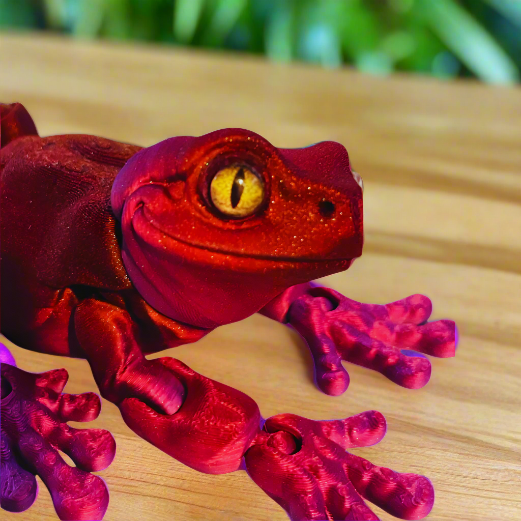 Side view of a 3D printed tree frog in red and purple, showing its elongated body and detailed legs, highlighting the vibrant color contrast.