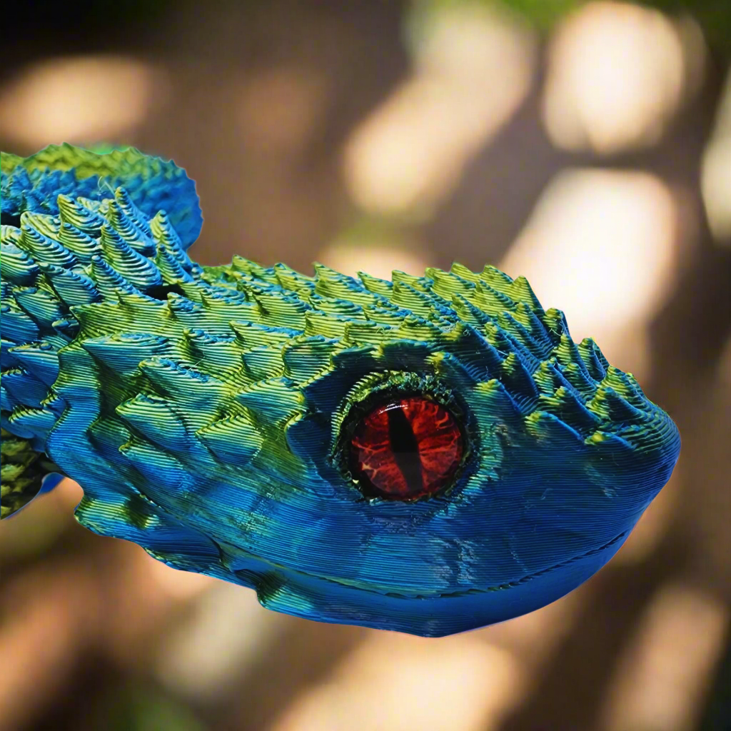 Close-up of a 3D printed copperhead snake toy's head, featuring intricate blue and yellow scale details and lifelike red eyes.