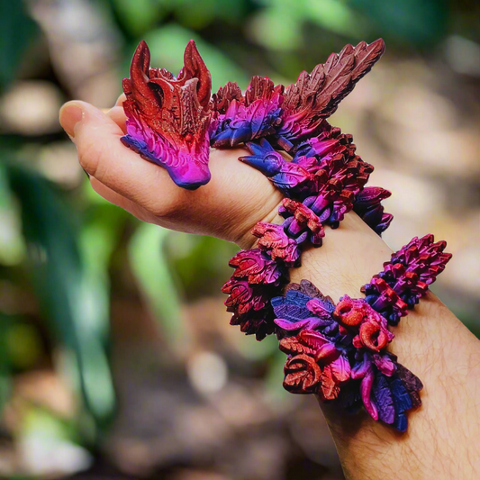 3D printed crystal-wing articulated dragon toy in galaxy red, blue, and purple, wrapped around a person's arm, showing its flexible and lifelike design, 23 inches long.