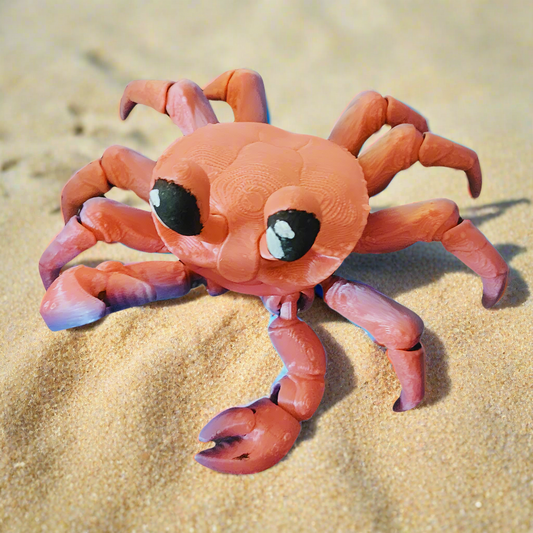 A front view of a cute, articulated 3D-printed crab in red and purple tones, resting on sand. The crab features large eyes and movable legs and claws, perfect as a fidget toy or collectible figurine.