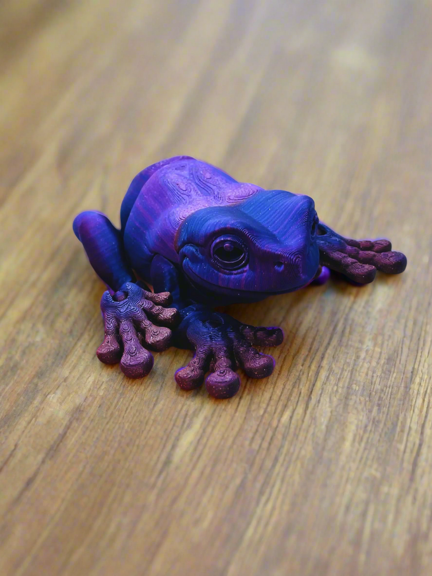 A 9-inch 3D printed tree frog in blue and purple, held in a hand to show scale, featuring a smooth eyeless face and detailed body.