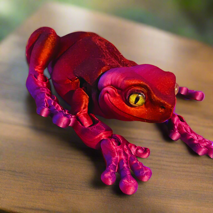 A 3D printed red and purple tree frog held in a hand to display its size, featuring large eyes and a smooth, detailed surface.