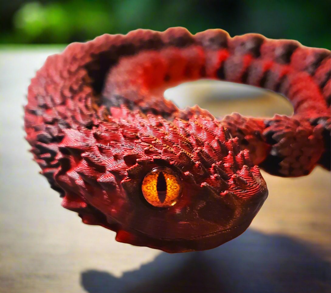 A detailed close-up of a red and black snake figure's head, showcasing its vivid orange eye and rough textured scales.
