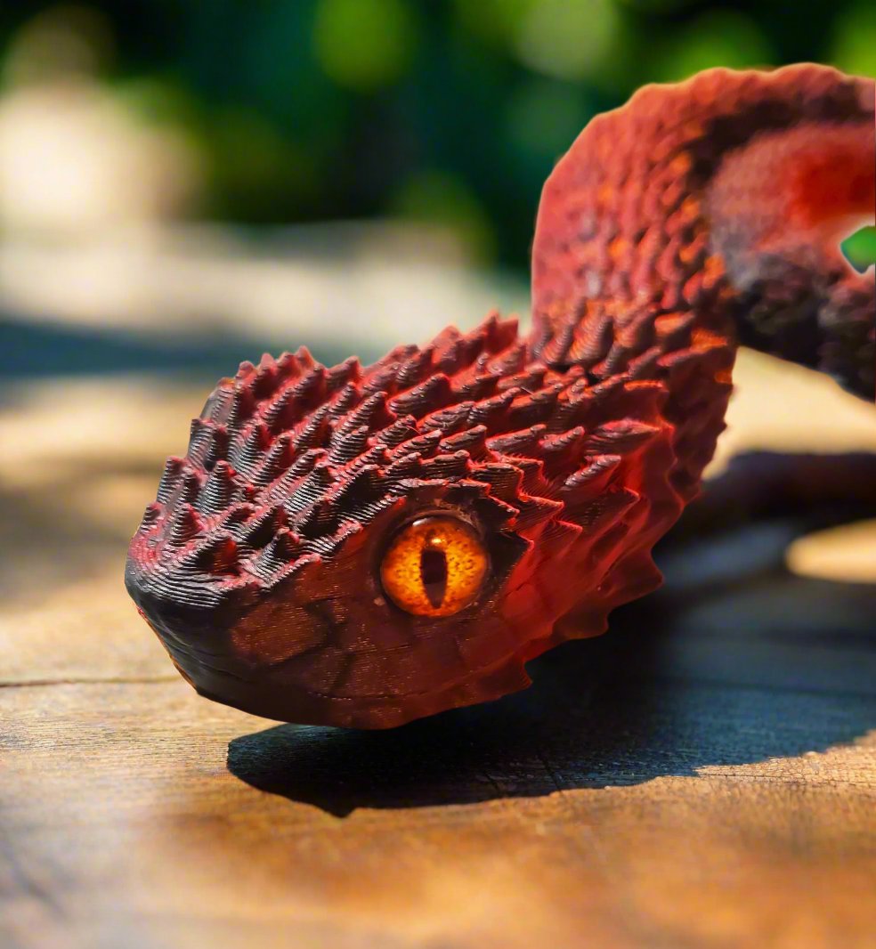 The head of a red and black snake figure, featuring its lifelike amber eye and a close-up view of its sharp, detailed scales.