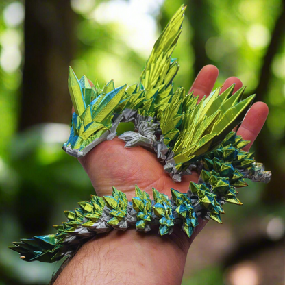 A full view of the green and blue dragon figurine, resting on a hand, showcasing its entire body, from wings to tail.