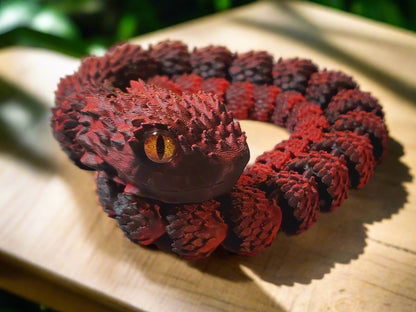 A full view of a coiled red and black snake figure with a vivid orange eye, showing the figure’s elaborate texture and shading.