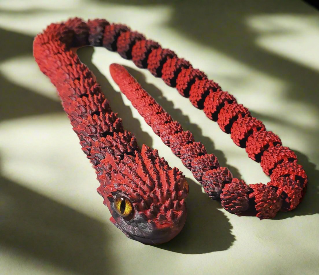  A red and black snake figure fully stretched out, showcasing its detailed body scales and lifelike amber eye, on a light background.
