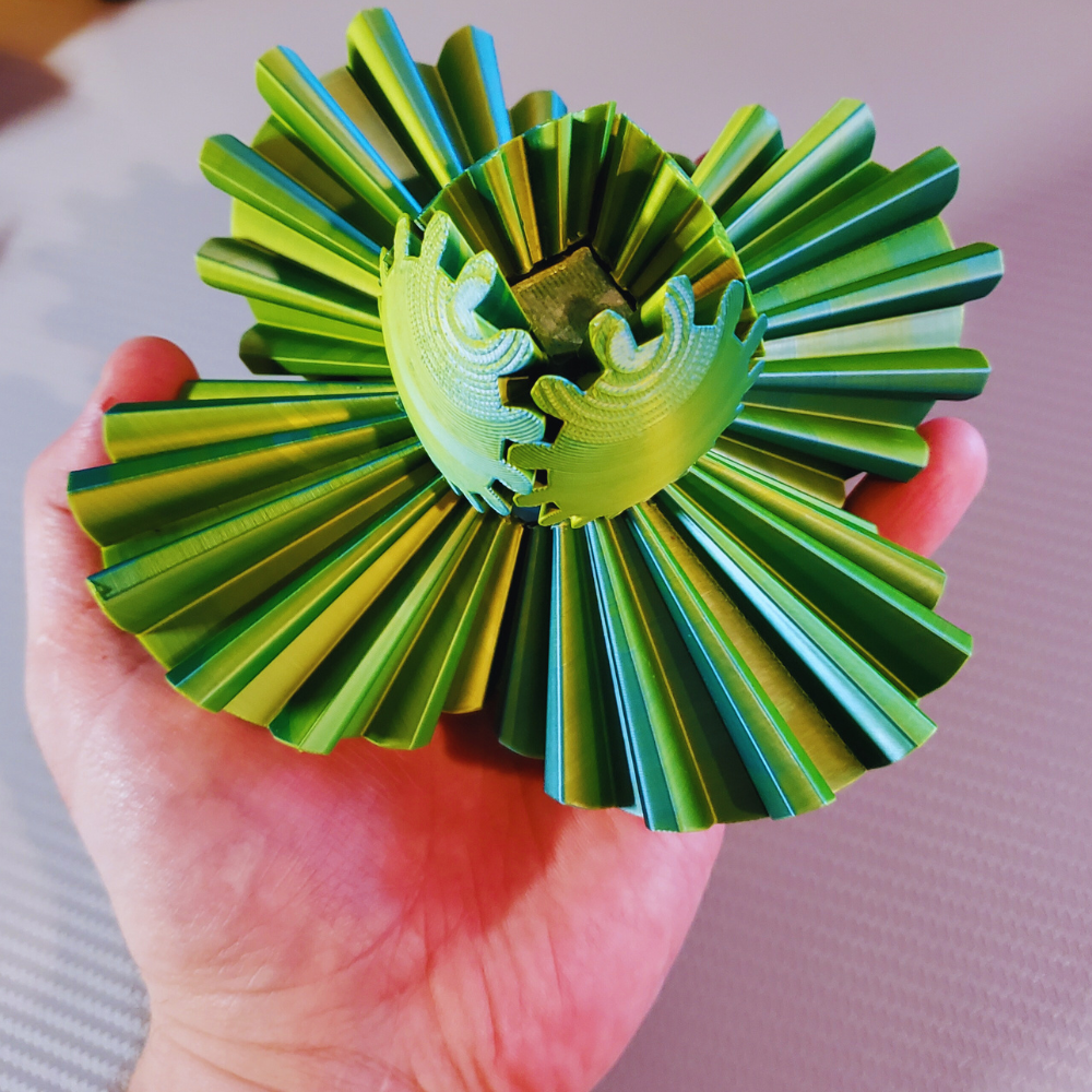 Close-up of a hand holding an open Gear Sphere 3D Printed Fidget Toy, showcasing the intricate gear mechanism in vibrant green and blue colors. Ideal for sensory engagement, stress relief, and enhancing focus.