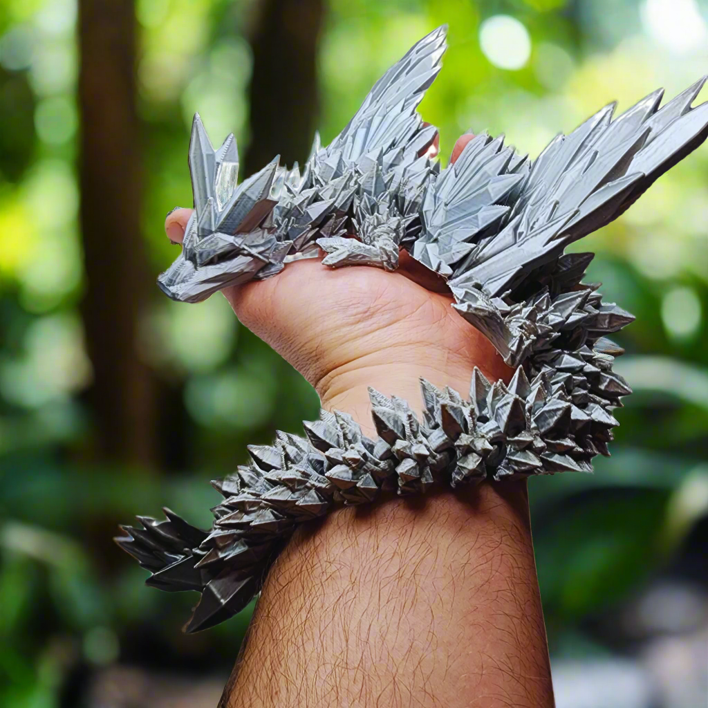 A hand holding a silver 3D-printed dragon figurine, focusing on its detailed texture and wing structure.