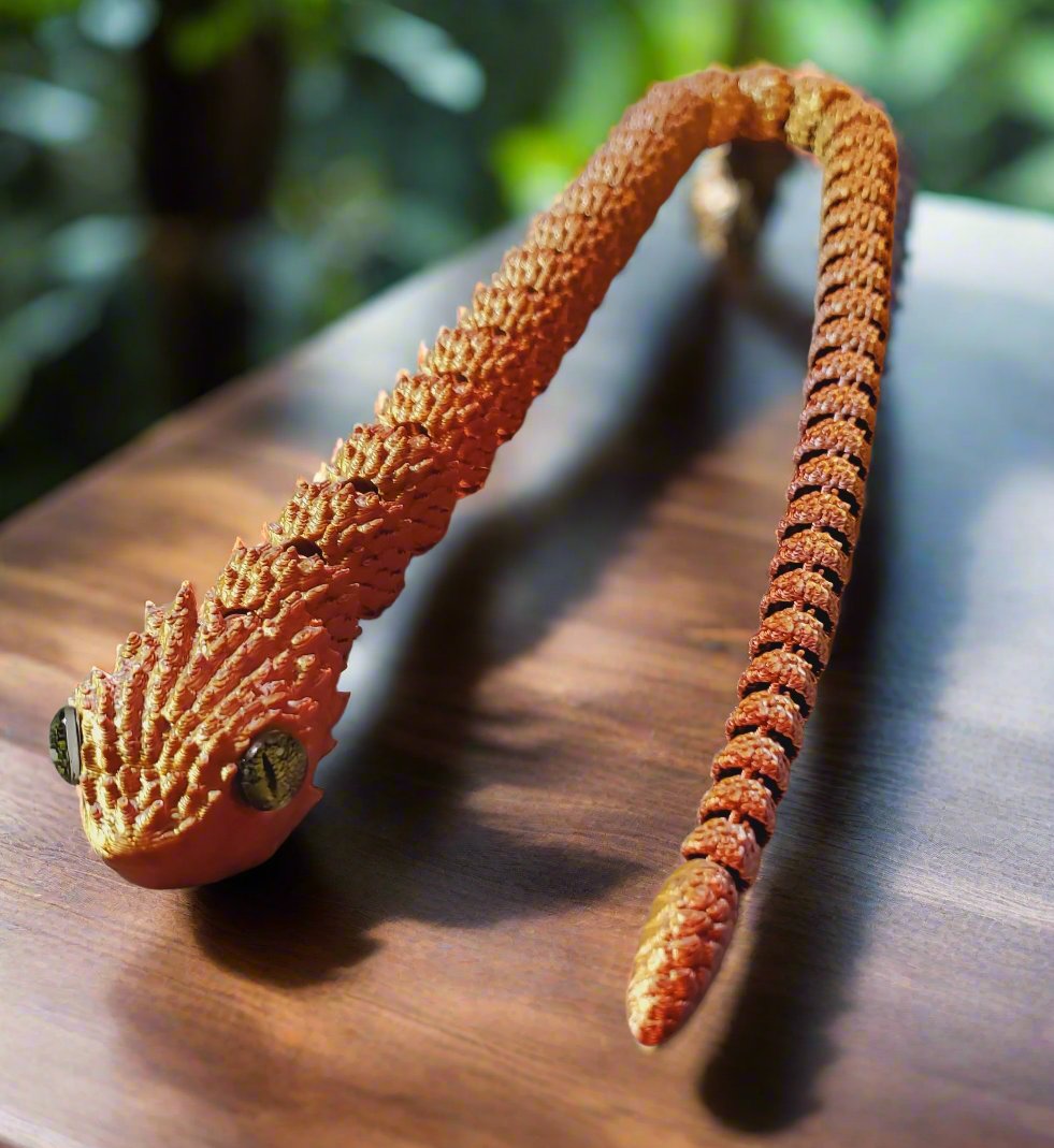 A stretched-out golden snake figure with lifelike amber eyes, showcasing intricate scales along its articulated body on a light surface.