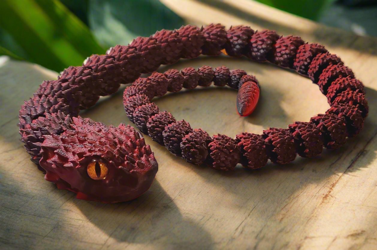 A long, uncoiled red and black snake figure with its vibrant orange eye standing out, displayed on a light-colored surface.
